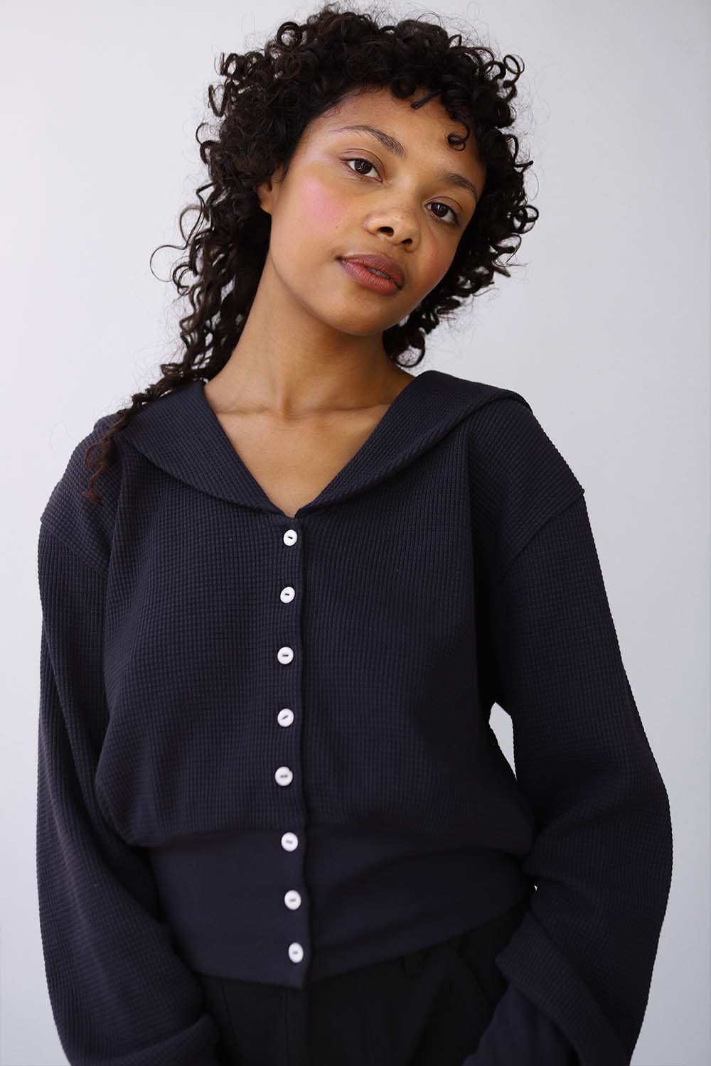A woman wearing a black sailor-inspired cardigan with white coconut buttons against a plain background
